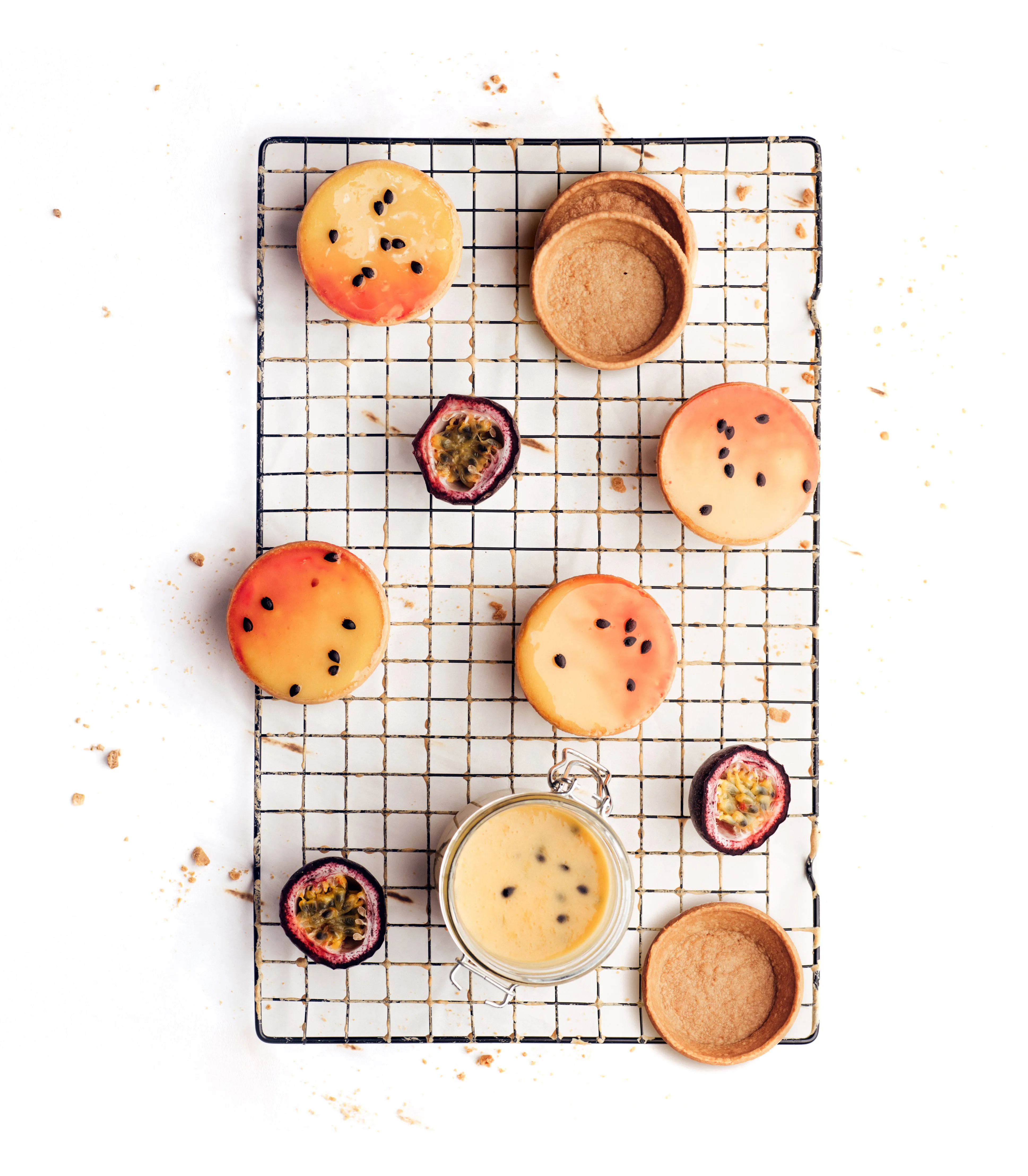 Passion fruit tarts and custard on a wire cooling rack, halved passion fruit scattered between them.